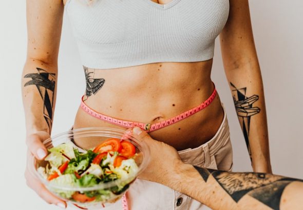 Fit woman measuring waist while holding a healthy salad bowl
