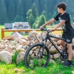 A young boy rides a mountain bike in Bukovel, Ukraine with a scenic forest backdrop.