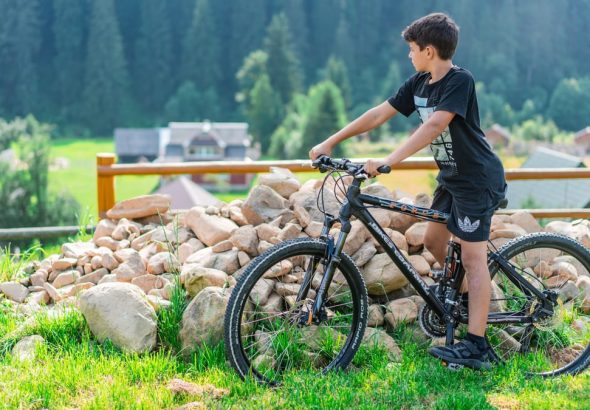 A young boy rides a mountain bike in Bukovel, Ukraine with a scenic forest backdrop.
